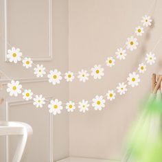 a woman is hanging daisies on a string in a room with a chair and table