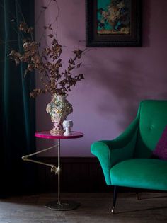 a green chair sitting next to a table with a vase on it and flowers in the corner