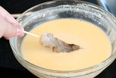 a person dipping something into a bowl with a toothpick in it's mouth