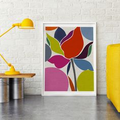 an art print on a white brick wall next to a yellow chair and table lamp