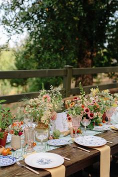 a long table with plates and flowers on it is set for an outdoor dinner party