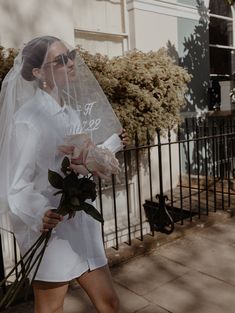 a woman walking down the street with a veil on her head and flowers in her hand