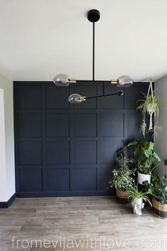 a room with some plants and lights on the ceiling, in front of a black paneled wall