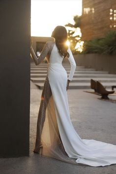 a woman in a long white dress leaning against a wall