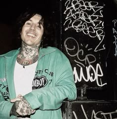 a man with tattoos standing in front of graffiti covered walls