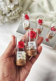 three small glass bottles with red roses in them and some pearls on the bottom one