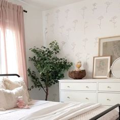 a bedroom with a bed, dresser and potted plant in the corner next to it