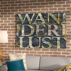 a living room with brick walls and a gray couch in front of the wall is a large wooden sign that says wander just