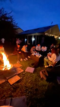 people are sitting around a fire pit in the yard at night, while others sit and watch