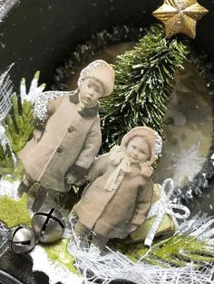 two small dolls sitting on top of a table next to a christmas ornament