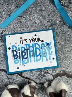 a happy birthday card with cotton balls and blue ribbon hanging from a hook on the ground