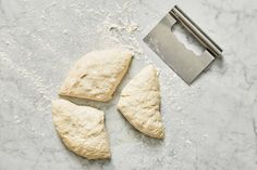 three uncooked pieces of bread next to a knife on a marble counter top