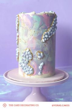 a cake decorated with white and blue flowers on a plate in front of a purple background