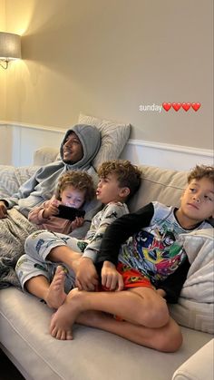 four children sitting on a couch looking at a cell phone