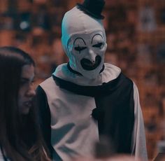 a person wearing a clown mask standing next to another person