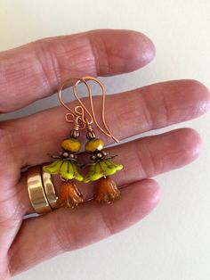 "Adorable new Czech glass premium flower earrings in chartreuse green and orange opaline with mustard yellow and copper accents. Opaque chartreuse Czech glass bellflowers with copper Picasso finish are accented with little Czech glass lilies in burnt orange opaline with metallic copper wash and mustard yellow Picasso rondelles. Wire wrapped in bright copper with copper accents. Ear wires are handmade German copper. Total drop is 1 3/4\"." Orange Flower-shaped Adjustable Earrings, Green Czech Glass Flower Earrings, Green Flower-shaped Glass Jewelry, Green Glass Flower-shaped Jewelry, Green Earrings With Flower Charm For Jewelry Making, Yellow Czech Glass Earrings For Gifts, Yellow Glass Earrings For Gift, Unique Yellow Czech Glass Jewelry, Nickel-free Yellow Czech Glass Earrings