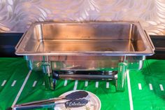 a stainless steel sink sitting on top of a green tablecloth covered floor next to a plate with utensils