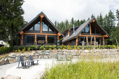 two chairs are sitting in front of a large house with stone walls and tall pine trees