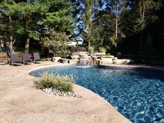 a pool surrounded by trees and rocks with a waterfall in the middle, next to lounge chairs