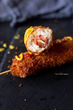 a piece of fried food on a stick with corn kernels and ketchup