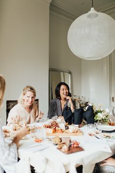 three women sitting at a table with food in front of them and one woman talking on the phone