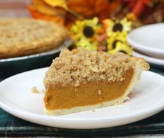 a slice of pumpkin pie on a white plate next to other plates with flowers in the background