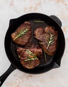 steaks in a cast iron skillet with rosemary garnish on the side