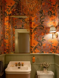 a bathroom decorated in orange and green with a white toilet, sink, mirror and chandelier