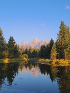 a lake surrounded by trees with mountains in the background and blue sky reflected in the water