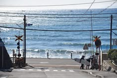 two people holding surfboards standing on the side of a road next to the ocean