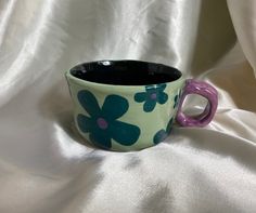 a blue and purple flowered cup sitting on top of a white cloth