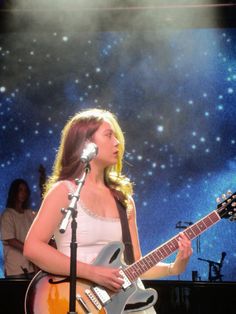 a woman holding a guitar while standing in front of a microphone