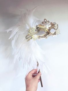 This Beautiful, bold and regal masquerade mask is on a handheld stick and decorated with fine shimmers and crystals and option to embellish with large Feather design. We specialize in customizing masquerade masks to match your event themes and outfit colors. Choose from a variety of masks patterns and we will customize it any color paints, feathers, shimmers and jewels to create an elegant custom masquerade mask for you! Quick processing and expedited shipping available on all orders, let us kno Masquerade Mask With Feathers, Masquerade Ball Outfit, White Masquerade Mask, White Masquerade, Elegant Face Mask, Masquerade Ball Masks