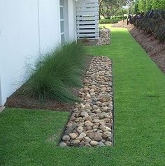 there is a long line of rocks in the grass next to a white wall and door