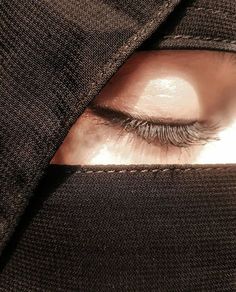 a woman's eye with long lashes is seen through the fabric on her coat