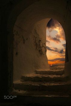 the sun is setting through an arch in a stone building with steps leading to it