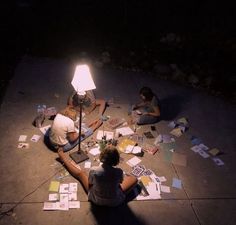 two people sitting on the ground in front of a lamp with papers all over them