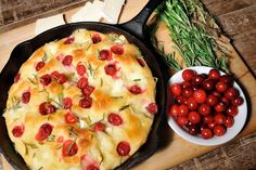 a skillet with tomatoes, cheese and bread in it on a wooden cutting board