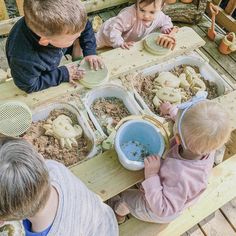 three children are sitting at a table playing with sand and water in their hands while another child looks on