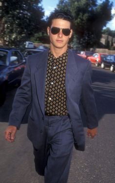 a man in a suit and tie walking down the street with sunglasses on his head