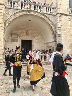 men and women dressed in historical costumes walking towards an entrance to a building with people on it