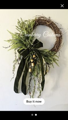 a green wreath with bells and greenery hanging from it's side on a white wall