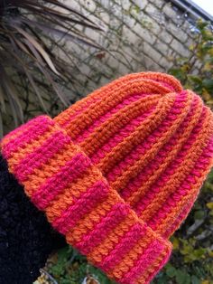 an orange and pink knitted hat on someone's arm