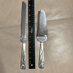 two knives and a fork sitting next to a ruler on top of a leather surface