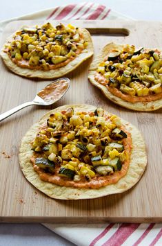 four flat bread pizzas with toppings on a cutting board