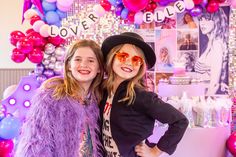 two girls standing next to each other in front of balloons