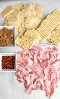 several different types of cheeses and crackers on a white tablecloth with other ingredients