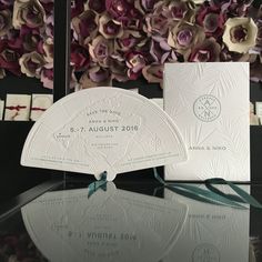 the wedding card is on display in front of some purple and white flowers with green ribbon