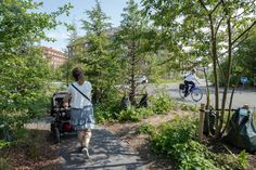 a woman walking down a path next to a forest filled with trees and people on bicycles