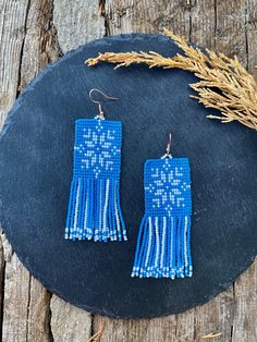 the blue beaded fringe earrings are sitting on top of a black stone slab next to some dry grass